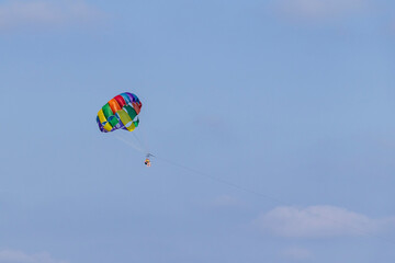 Two people enjoy parasailing high above the ocean, surrounded by a clear blue sky. The colorful...