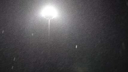 A street light is lit up in the dark. The sky is cloudy and the snow is falling - Powered by Adobe