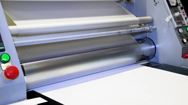An industrial laminator works by laminating, applying a transparent film to paper in the production room of a printing house