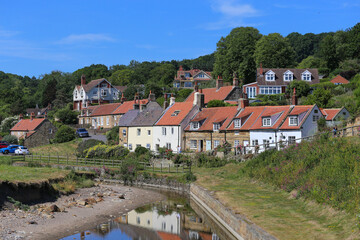 A picturesque seaside village nestled among trees. Red-roofed cottages line a shallow stream and...