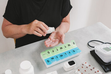An elderly woman pours one tablet from a bottle into her palm.