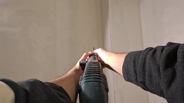 pov Construction worker drilling wall using rotary hammer drill and chisel