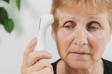 An elderly woman measures her temperature using a non-contact thermometer.