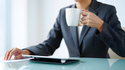 Businesswoman in gray suit reviewing documents, holding coffee mug, modern office setting.