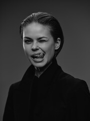 Obraz premium Black and white portrait of a winking woman with playful expression wearing dark clothing against simple dark background in studio lighting.