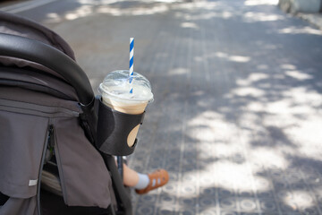 Iced coffee in a plastic cup with striped straw placed in a stroller cup holder on a sunny urban sidewalk
