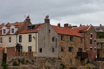 A landscape image showing a row of rustic houses. The houses are varied in style and construction,...