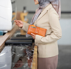 A woman's body wearing a hijab and formal attire stands in front of the reception desk holding a...