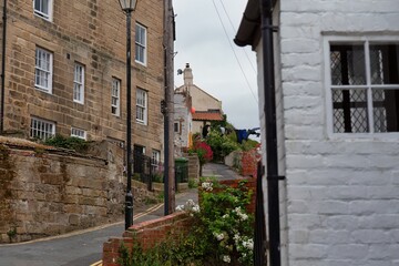 A quaint street view shows a stone building on the left, and a white building on the right, creating a sense of depth and charm  in Staithes - North Yorkshire - United Kingdom