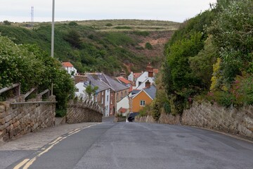 A view down a road towards a cluster of houses nestled in a green, hilly landscape  in Staithes - North Yorkshire - United Kingdom