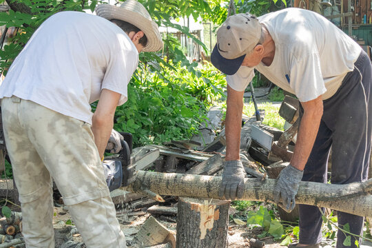 Two men working together to cut a log with a chainsaw outside.