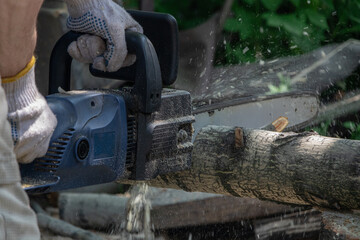A man is using a chainsaw to cut a log, creating a flurry of sawdust.