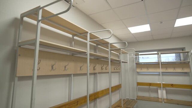 Empty illuminated locker room equipped with benches shelves and hooks. Place to keep personal stuff and accessories in modern sports center