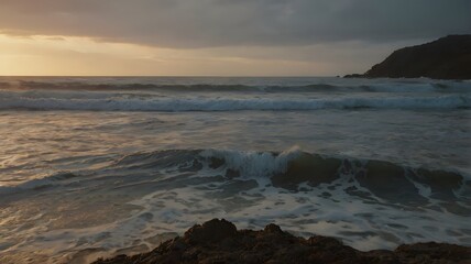 Un atardecer nublado en la costa, con olas espumosas rompiendo sobre la arena oscura y rocas en primer plano. El cielo se ti&ntilde;e de suaves tonos naranjas y grises.