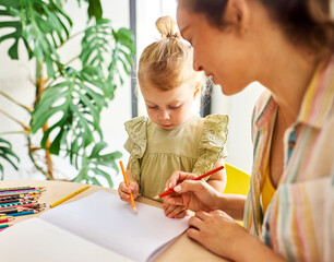 Portrait of a little girl and mother or teacher coloring a book in classroom or at home. Education and development concepts