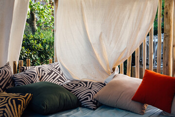 Coussins et oreillers sous un voilage de pergola. Lieu de repos et de relaxation. Rideaux blanc et oreillers confortables pour une ambiance zen. Pergola en &eacute;t&eacute;.