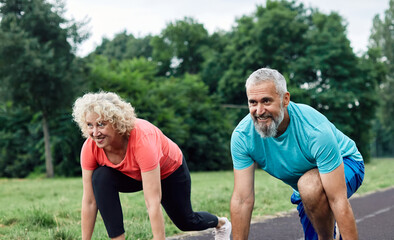 Smiling active mid aged couple standing in start position,  jogging running and walking doing...