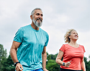 Smiling active mature middle aged couple jogging together in the park