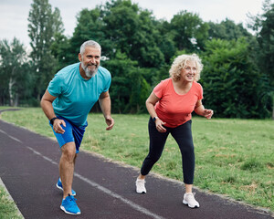 Smiling active mid aged couple standing in start position,  jogging running and walking doing...