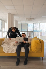Two Caucasian men discussing work on a laptop while sitting on a sofa. Modern office. 