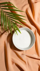 Stock photo of coconut milk in bowl with palm leaf on peach silk background studio shot