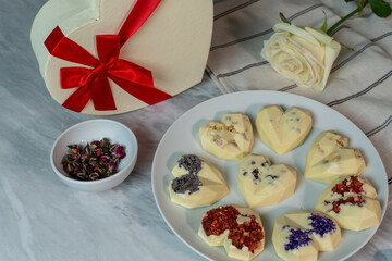Heart-shaped chocolates with floral decoration on marble table with rose and gift box