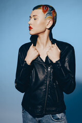 Woman with shaved colorful hair wearing black leather jacket and blue jeans stands confidently...