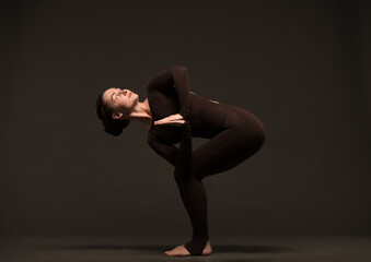 professional yoga girl doing exercises on dark background.young lady in brown sportswear on dark...