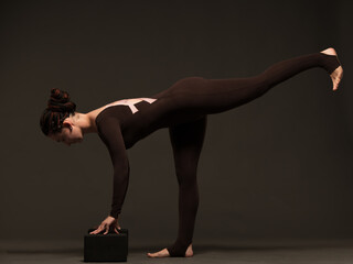 professional yoga girl doing exercises on dark background.young lady in brown sportswear on dark...