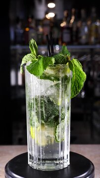 Glass with moxito cocktail rotating on bar counter. Vertical screen
