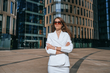 A focused professional woman in a white suit reads a tablet against a backdrop of towering urban glass facades, depicting modern ambition.