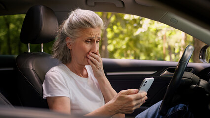 Naklejka premium Shocked upset scared Caucasian elderly aged woman female car driver client user holding mobile phone smartphone shock receiving bad news cellphone scam app error trouble upset worry inside automobile
