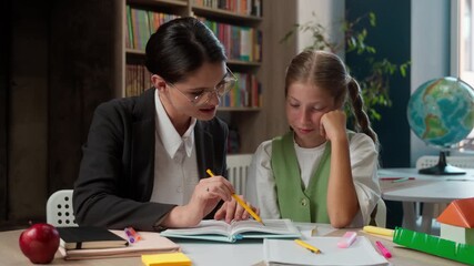 Caucasian woman teacher female professor teaching happy little girl schoolgirl child school kid pupil learner student reading task homework learning studying looking at camera inside classroom library - Powered by Adobe