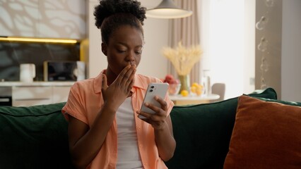 Upset shocked frustrated African American ethnic business woman female girl lady businesswoman user client hold mobile phone smartphone shaking head no bad betting losing money gambling error at home