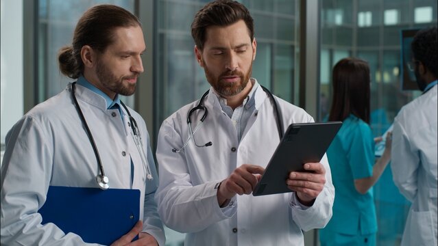 Experienced Caucasian two men doctors clinician surgeon pediatrician physician in labcoat stethoscope examining patient health test result using digital tablet diagnostic treatment at hospital clinic