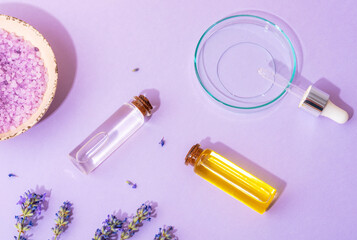 Lavender bath salt in bowl, lavender flowers, aromatic oil and facial serum in petri dish with...