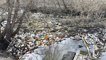 Dirty river is polluted with many plastic bottles. A lot of trash is dumped in open and freely...