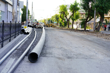 Road construction underway with large pipes and heavy machinery in a city setting during daylight hours