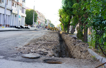 Construction work underway on urban road with excavation for utility installation in a city neighborhood during daylight hours