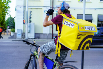 Fototapeta premium Delivery cyclist takes a break to hydrate in the city on a warm afternoon while waiting for the next order