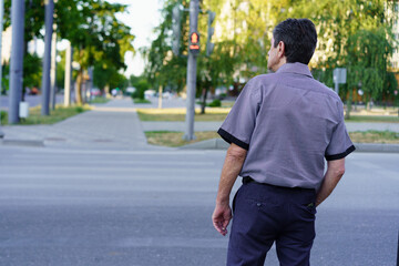 Obraz premium Man waiting at a crosswalk in a quiet urban area during the daytime