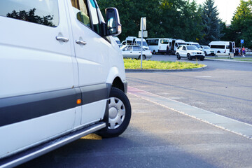 White vans parked in a transportation hub during daylight near trees and other vehicles in the...