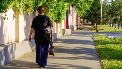Woman walking along tree-lined sidewalk in a quiet neighborhood during late afternoon