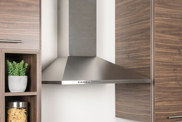 Close-up of modern stainless steel range hood surrounded by walnut cabinets, white wall, and open...