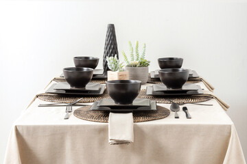 Rustic chic inspired symmetrical table setting with matte black dinnerware, textured woven...