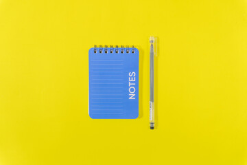 Flat lay of a pen and notebook on a vibrant yellow background