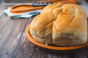 A loaf of bread served on a wooden plate placed on a rustic wooden surface