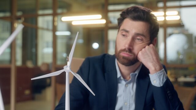 Upset frustrated Caucasian business man looking windmill thinking typing laptop at office businessman male guy engineer entrepreneur wind turbine working online computer pensive ecology green power