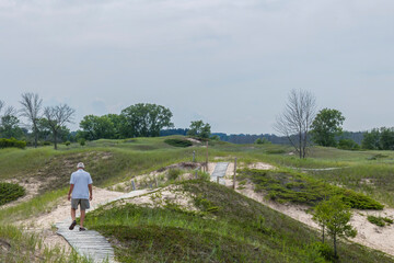 A man walking on a boardwalk over sand dunes at Kohler-Andre State Park in Wisconsin. 