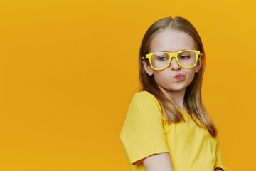 A cute girl wearing yellow glasses and a matching yellow t shirt, making a playful expression...